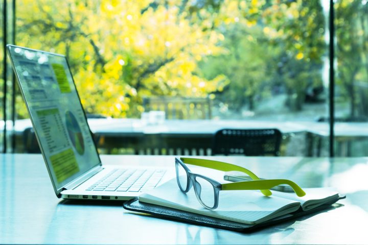 Laptop, Brille und Notizbuch vor einem grünen Hintergrund